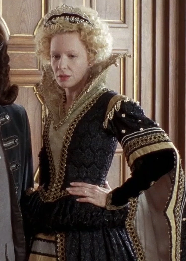 Sunnyi Melles as Königsmutter (The King's Mother) wearing a black and gold gown in the 2009 film "Sechs auf einen Streich: Die kluge Bauerntochter" (Finest Fairy Tales: The Peasant's Wise Daughter).