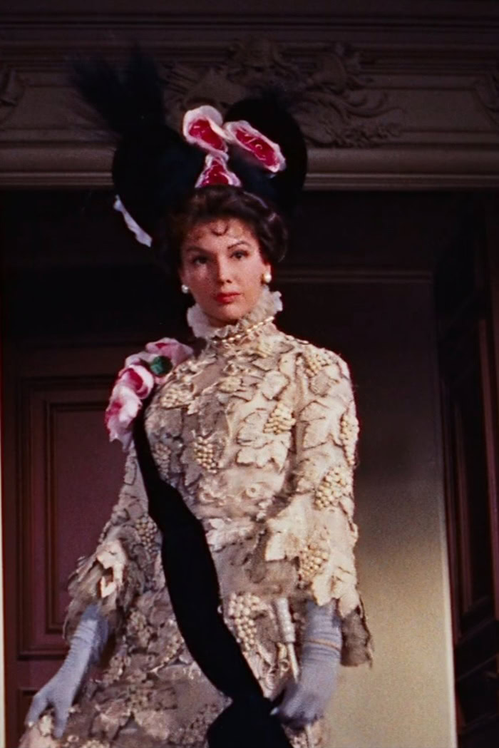 An uncredited actress wearing a white lace dress patterned with leaves and grapes in the 1958 film "Gigi."
